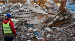 Construction worker in protective wear standing in front of rubble.